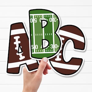 Puede incluir: Tres letras troqueladas A, B y C. La letra A es marrón con cordones y rayas blancas de balón de fútbol americano. La letra B es verde con líneas de campo blancas y los números 30 y 50. La letra C es marrón con rayas y cordones blancos.