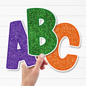 Könnte beinhalten: Drei glitzernde ausgeschnittene Buchstaben, bestehend aus einem violetten A, einem grünen B und einem orangefarbenen C. Jeder Buchstabe hat einen dicken weißen Rand und eine texturierte, funkelnde Oberfläche als dekorative Einzelstücke.