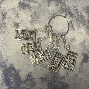 May include: Five silver-toned stitch markers shaped like £100 notes. Each marker has a ring attached to the top for easy use.