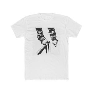 May include: A white short-sleeve t-shirt featuring a black and white graphic print on the chest. The graphic depicts a pair of feet wearing inline skates, with one skate positioned on a metal handrail and the other suspended in the air.