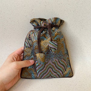 Puede incluir: Una peque&ntilde;a bolsa de cord&oacute;n hecha de tela marr&oacute;n con un dise&ntilde;o estampado azul y dorado. La bolsa tiene un cord&oacute;n marr&oacute;n y est&aacute; atada en la parte superior.