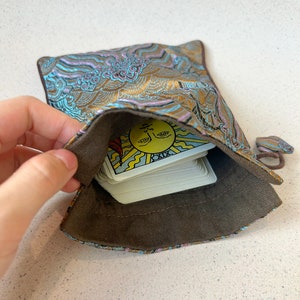 Puede incluir: Una baraja de tarot con una bolsa de patr&oacute;n dorado y azul. La carta superior es la carta del Sol, que es la 19&ordf; carta del Arcano Mayor.