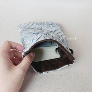 Puede incluir: Una bolsa de tela con estampado blanco y azul con forro de terciopelo marr&oacute;n. La bolsa est&aacute; abierta y dentro hay una baraja de cartas. La carta superior tiene un solo car&aacute;cter chino.