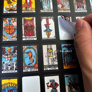 May include: A set of tarot cards with colorful illustrations and black borders. The cards are arranged in a grid pattern on a black background. The cards are labeled with their names, such as "The Fool", "The Magician", "The High Priestess", "The Empress", "The Emperor", "Wheel of Fortune", "Justice", "The Hanged Man", "Judgement", "The World", and "Ace of Cups".