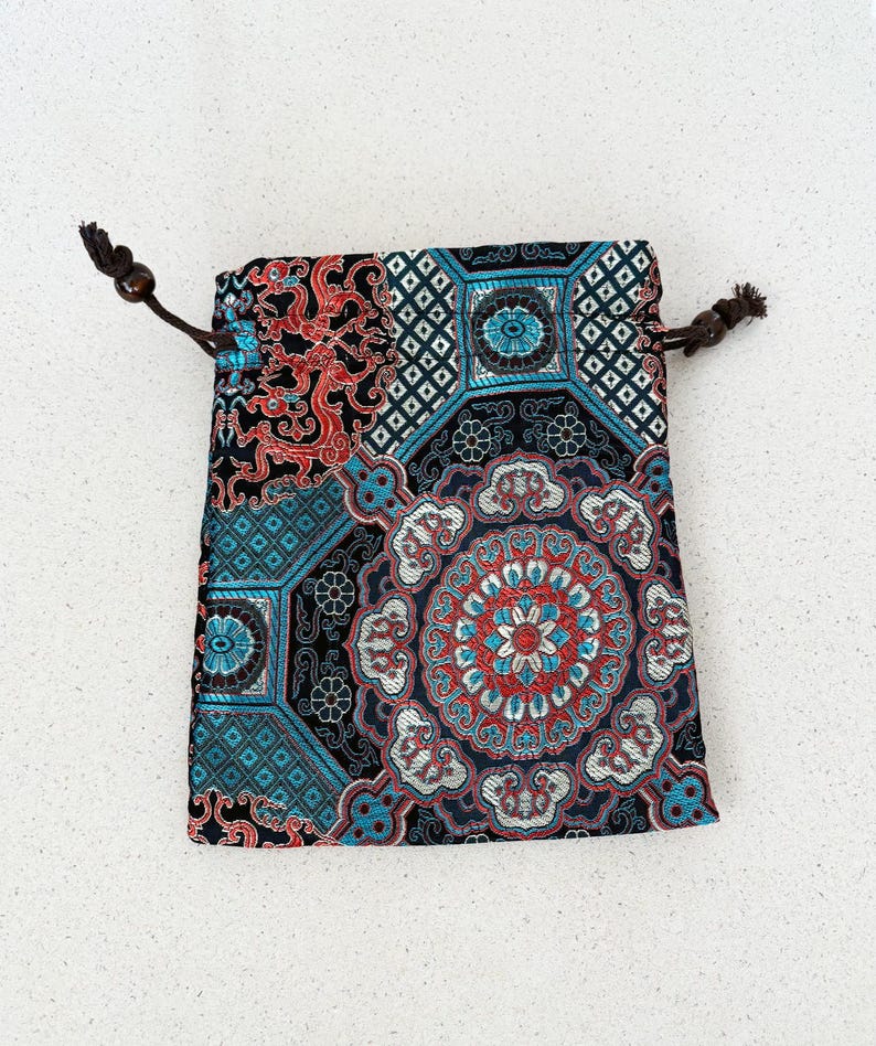 May include: A small, patterned drawstring bag. The bag features a detailed design with teal, red, and white floral and geometric patterns on a black background. The drawstring is brown.