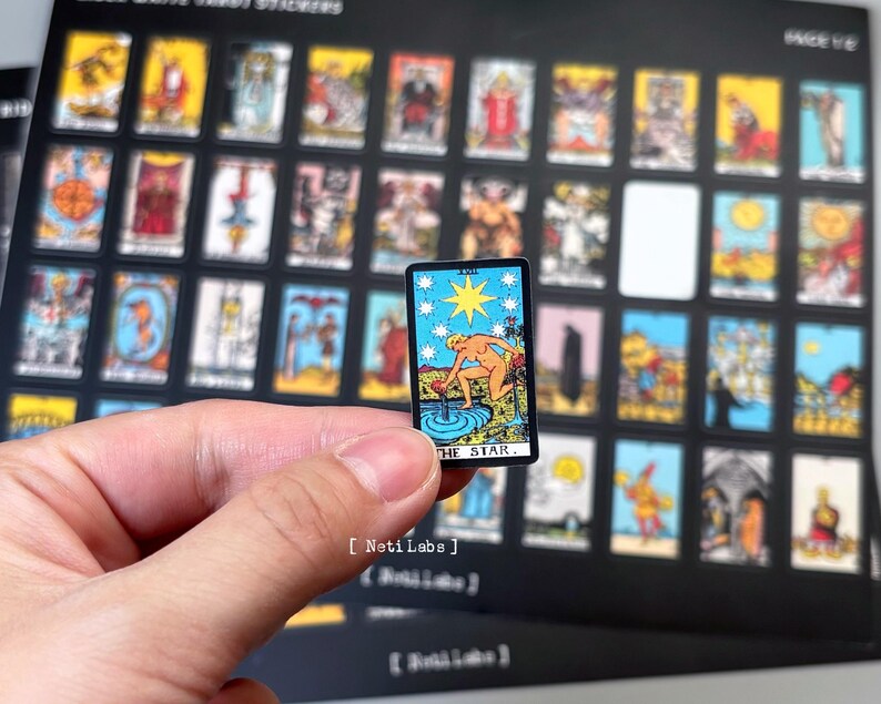 May include: A close-up of a tarot card with a woman pouring water from a pitcher into a pool. The card is titled "The Star" and has a blue, white, and yellow color scheme.