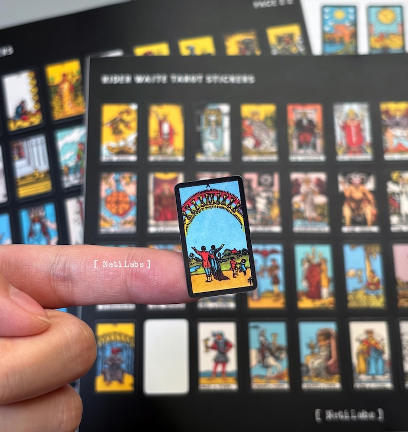 May include: A close-up of a tarot card sticker featuring the 'The World' card from the Rider Waite Tarot deck. The card depicts a woman standing with her arms outstretched, surrounded by a wreath of flowers and a blue sky with a yellow sun.