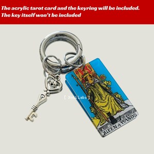 May include: A silver key charm attached to a silver keyring with a blue and white acrylic tarot card featuring the Queen of Wands. The card has a yellow and black illustration of a woman sitting on a throne with a staff and a black cat.