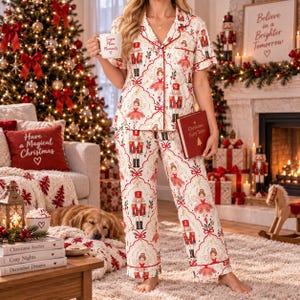 May include: A two-piece pajama set featuring a short-sleeved button-down shirt and matching pants with a white background and a repeating pattern of nutcrackers and ballerinas in red, gold, and green, accented by red piping along the edges.