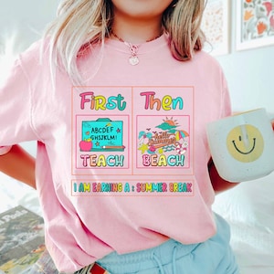 May include: Pink t-shirt with a graphic design that says "First I Teach Then I Beach" and "I am earning a: Summer Break".