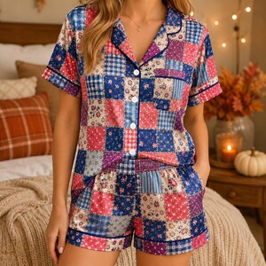 May include: A short-sleeve pajama set featuring a button-down shirt and matching shorts with a patchwork pattern. The fabric displays a mix of blue, pink, and white squares with floral, polka dot, and plaid prints, finished with dark blue piping.