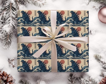 May include: Gift-wrapped present featuring a repeating pattern of a blue Godzilla monster with a red sun and ocean waves. The gift is tied with a cream-colored ribbon, set against a snowy background with pine branches and a Fast Shipping text.