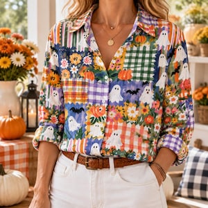 May include: A long-sleeve button-down shirt featuring a patchwork pattern of white ghosts, orange pumpkins, black bats, and colorful flowers on checkered and plaid backgrounds. The shirt has a classic collar and is tucked into white denim jeans.
