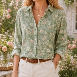 Puede incluir: Una camisa de manga larga con botones en color verde salvia claro con un denso estampado floral de pequeñas flores blancas, rosas y amarillas con follaje verde. La camisa está metida en un pantalón blanco sujeto por un cinturón de cuero trenzado.