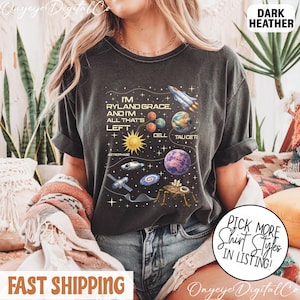 May include: Dark heather t-shirt with a space-themed graphic. The design includes a rocket ship, planets, and the text "I'm Ryland Grace, and I'm all that's left." The shirt also has the text "Cell Tauceti" and "Astrophage."