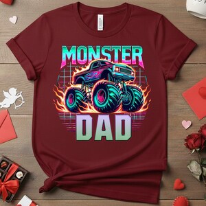 Peut inclure: T-shirt bordeaux avec un motif de monster truck, de grands pneus et des flammes. Le texte "MONSTER DAD" est affich&eacute; au-dessus et en dessous du camion dans un d&eacute;grad&eacute; de couleurs n&eacute;on. Le t-shirt a des manches courtes.