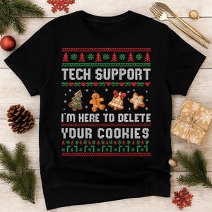 Może przedstawiać: Czarny t-shirt z świątecznym wzorem. Koszulka zawiera biały napis "TECH SUPPORT I'M HERE TO DELETE YOUR COOKIES", a także grafiki choinki, piernikowego ludzika, dzwonka i ciasteczka w kształcie płatka śniegu. Czerwone i zielone akcenty.