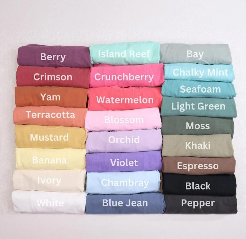 May include: A collection of folded fabric items in various colors, each labeled with a color name. Colors include Berry, Crimson, Yam, Terracotta, Mustard, Banana, Ivory, and White. Other colors are Island Reef, Crunchberry, Watermelon, Blossom, Orchid, Violet, Chambray, and Blue Jean.