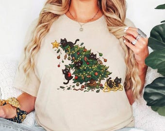 Op de afbeelding: Zandkleurig T-shirt met een grillig kerstboomontwerp. De boom is versierd met lichtjes, ornamenten en speelse zwarte katten. Een gouden ster staat bovenop de boom, en de woorden "Color - Sand" staan onderaan.
