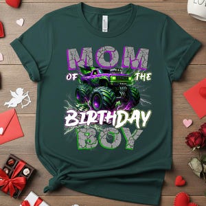 May include: Dark green t-shirt with a graphic that reads "MOM OF THE BIRTHDAY BOY." The graphic features a purple and green monster truck with lightning bolts. The text is in white and gray with a cracked effect.