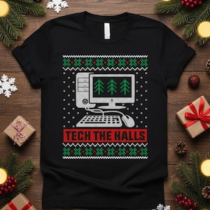 Op de afbeelding: Zwart T-shirt met een kerstontwerp met computerthema. Het ontwerp toont een computermonitor met drie kerstbomen, een toetsenbord en de tekst "TECH THE HALLS" in rood en wit.