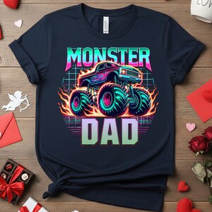 Peut inclure: T-shirt bleu marine avec un motif de camion monstre et le texte "MONSTER DAD". Le design comprend un camion monstre avec des flammes et des couleurs n&eacute;on, id&eacute;al comme cadeau.