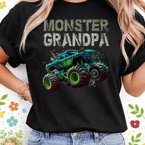 May include: Black t-shirt with the text "MONSTER GRANDPA" in distressed white and green lettering. The shirt features a graphic of a monster truck in shades of blue and green with large, green wheels.