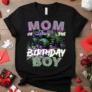 May include: Black t-shirt with a graphic of a monster truck in purple and green, with the text "MOM OF THE BIRTHDAY BOY" in white and green. The design includes lightning bolts and a checkered flag.