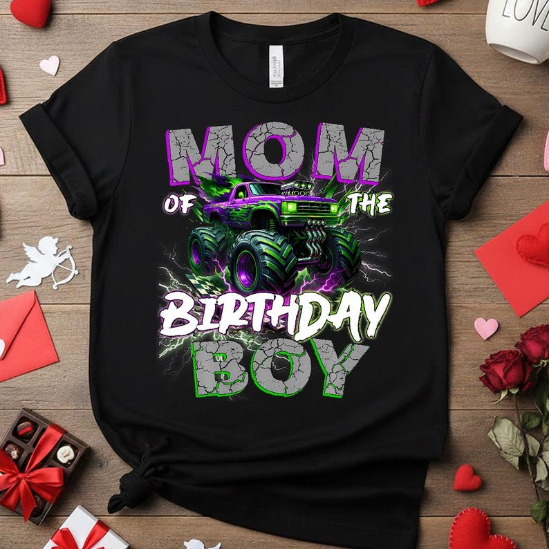 May include: Black t-shirt with a graphic of a monster truck in purple and green, with the text "MOM OF THE BIRTHDAY BOY" in white and green. The design includes lightning bolts and a checkered flag.