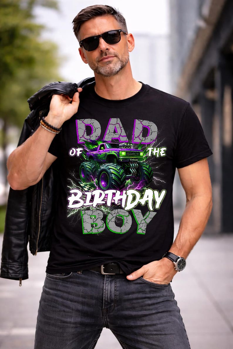 May include: Black t-shirt with a graphic of a monster truck in green and purple, with the text "DAD OF THE BIRTHDAY BOY" in a cracked stone style. The shirt is worn by a person wearing sunglasses.