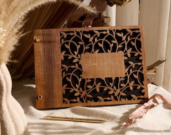 May include: A wooden guest book with a black background and a vine pattern. The book has a brass hinge and a brass clasp. The text "Blair & Mason 06.21.2021" is engraved on the front.