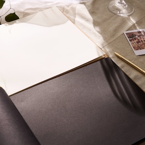 May include: A black and white photo album with a white page open and a gold pen lying on the table next to it.