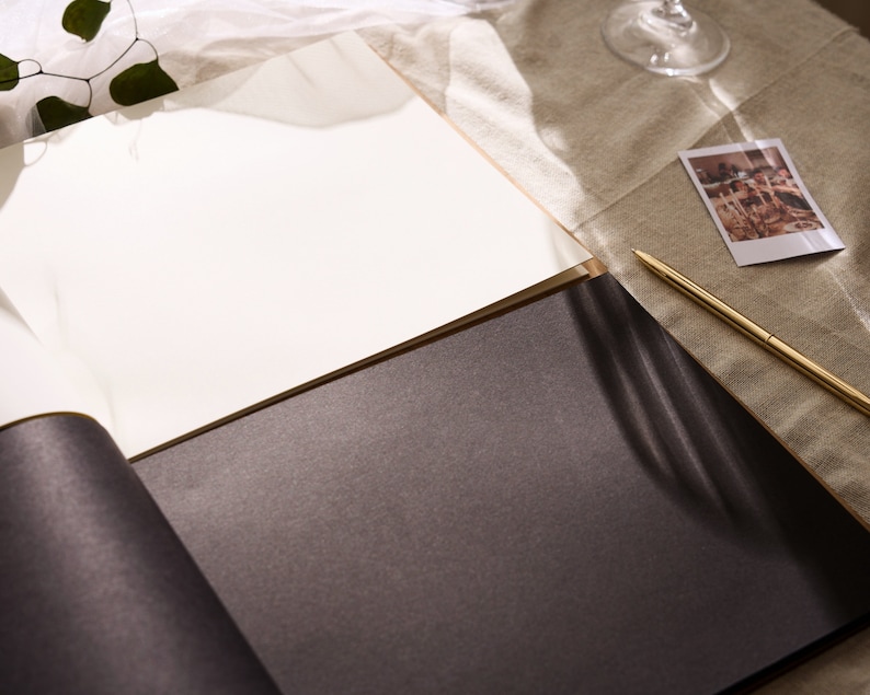 May include: A black and white photo album with a white page open and a gold pen lying on the table next to it.