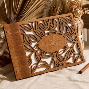 May include: A wooden guest book with a leafy design and the text "William & Sophia" and "Dec. 11th, 2022" engraved on the front.