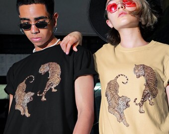 May include: Two people wearing t-shirts with a graphic print of two tigers facing each other. The person on the left is wearing a black t-shirt and the person on the right is wearing a yellow t-shirt.