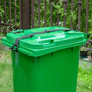 May include: A bright green plastic waste bin featuring a black adjustable strap secured across the lid. The strap includes a small black buckle and a white logo tag with the text ZUNSAN. The bin has a molded handle and a hinged lid design.
