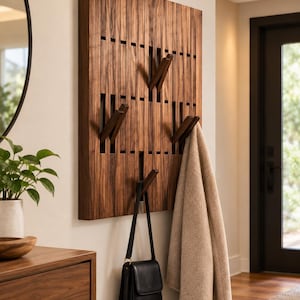 May include: A rectangular wall-mounted coat rack constructed from vertical dark brown wooden slats. The design features four retractable hooks integrated into the slatted surface, currently holding a beige coat and a black leather handbag.