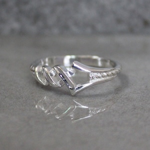 May include: A silver ring with a twisted band and a geometric design in the center.