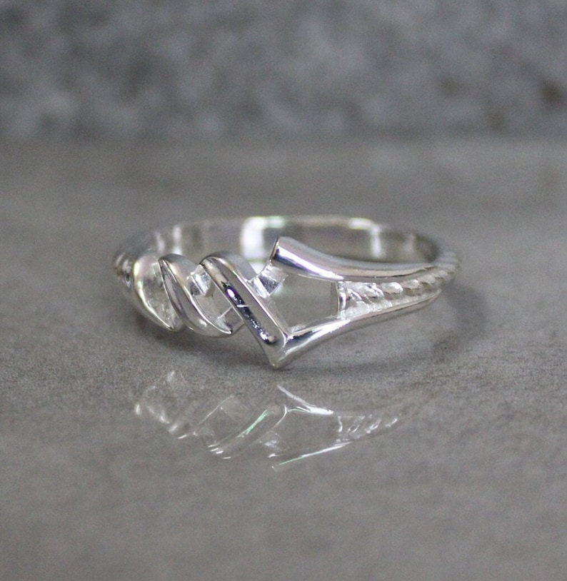 May include: A silver ring with a twisted band and a geometric design in the center.