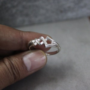 May include: A silver ring with a unique, geometric design. The band is twisted and the top of the ring features a geometric shape with an open center.