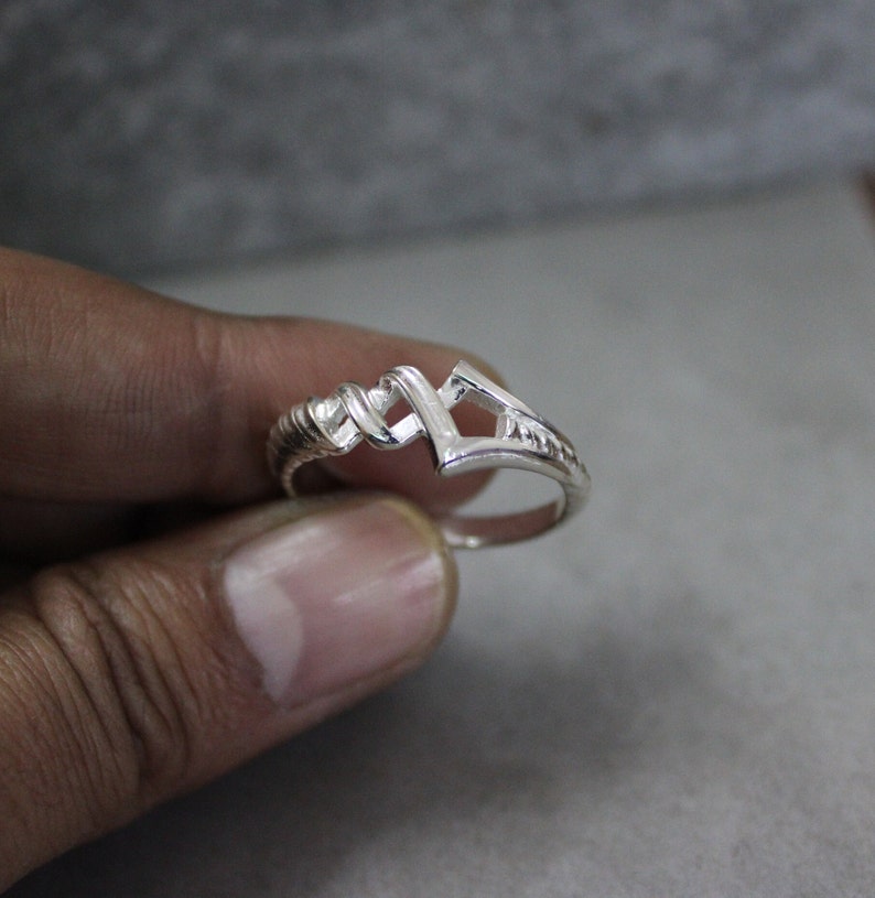 May include: A silver ring with a unique, geometric design. The band is twisted and the top of the ring features a geometric shape with an open center.
