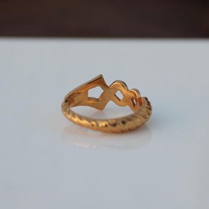 May include: A gold ring with a unique design featuring a series of interlocking loops. The ring has a textured band.