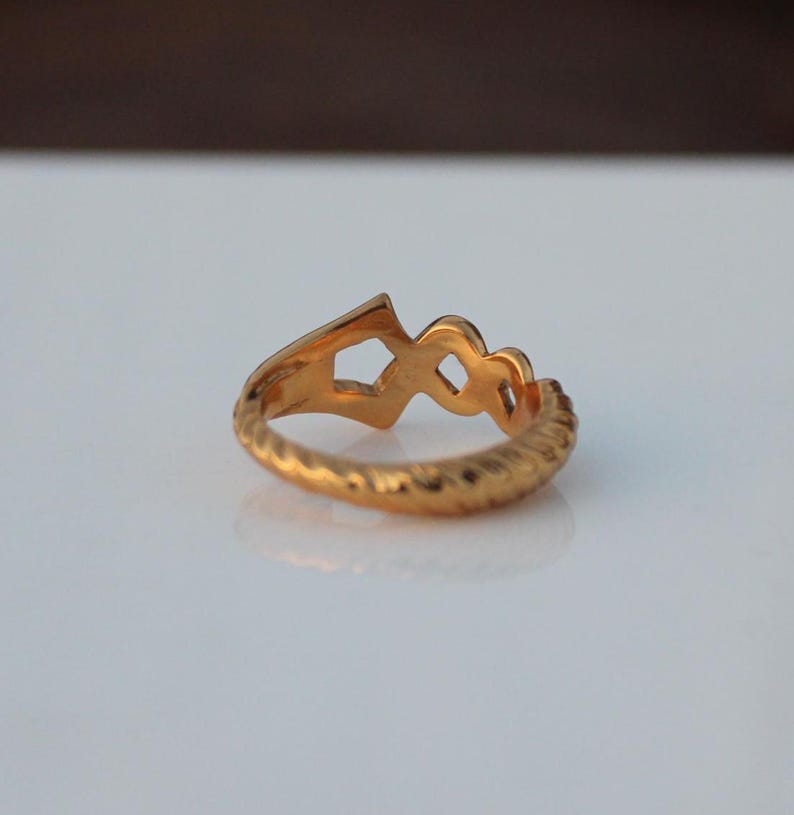 May include: A gold ring with a unique design featuring a series of interlocking loops. The ring has a textured band.