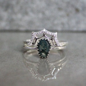 May include: A silver ring set with a green moss agate gemstone. The ring features a delicate, intricate design with small clear stones.