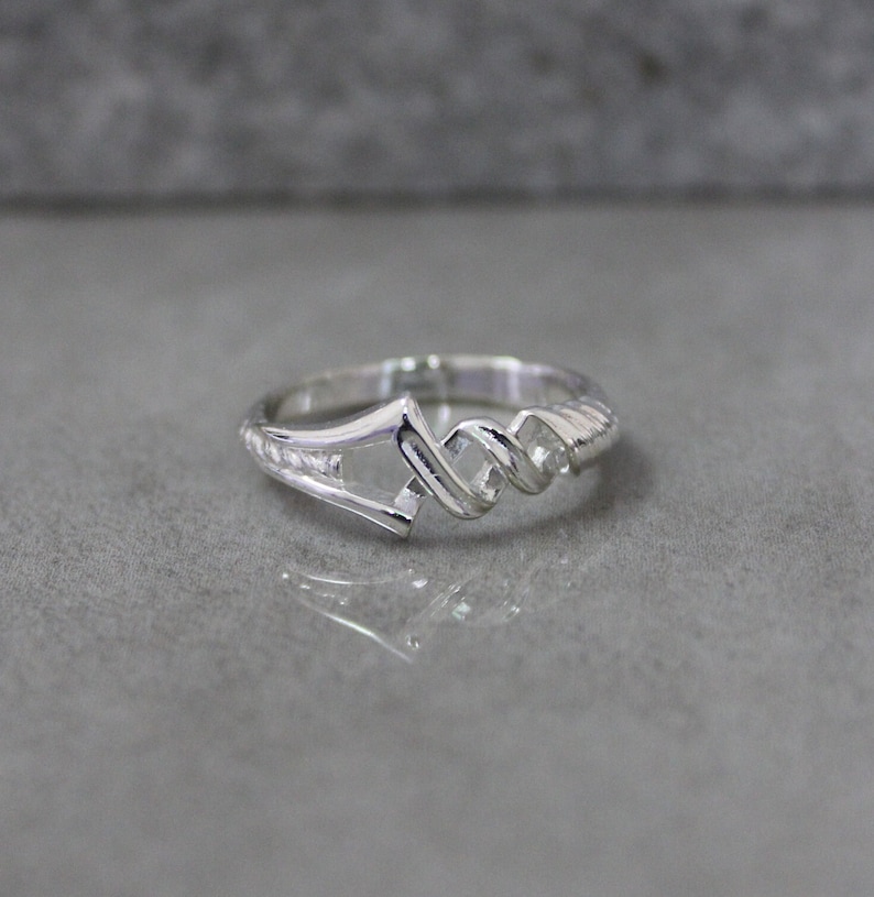 May include: A silver ring with a twisted design. The ring is open on one side and has a unique, geometric shape.