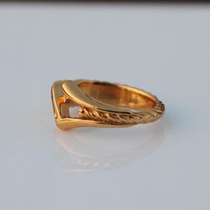 May include: A gold-toned ring with a unique design featuring a twisted band and a V-shaped cutout.
