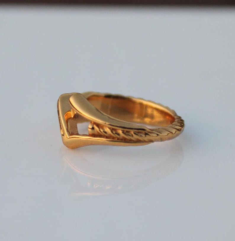 May include: A gold-toned ring with a unique design featuring a twisted band and a V-shaped cutout.