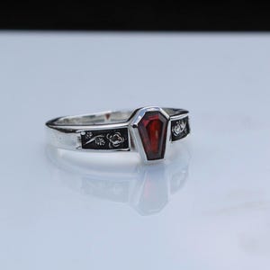 K&ouml;nnte beinhalten: Ein silberner Ring mit einem Sarg-f&ouml;rmigen, tiefroten Edelstein. Das Band ist mit floralen und Rankenmustern verziert. Das Design des Rings ist gotisch und einzigartig.