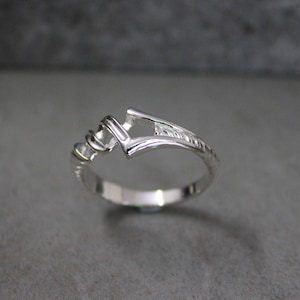 May include: A silver ring with a unique, open design. The band is twisted and has a textured finish.