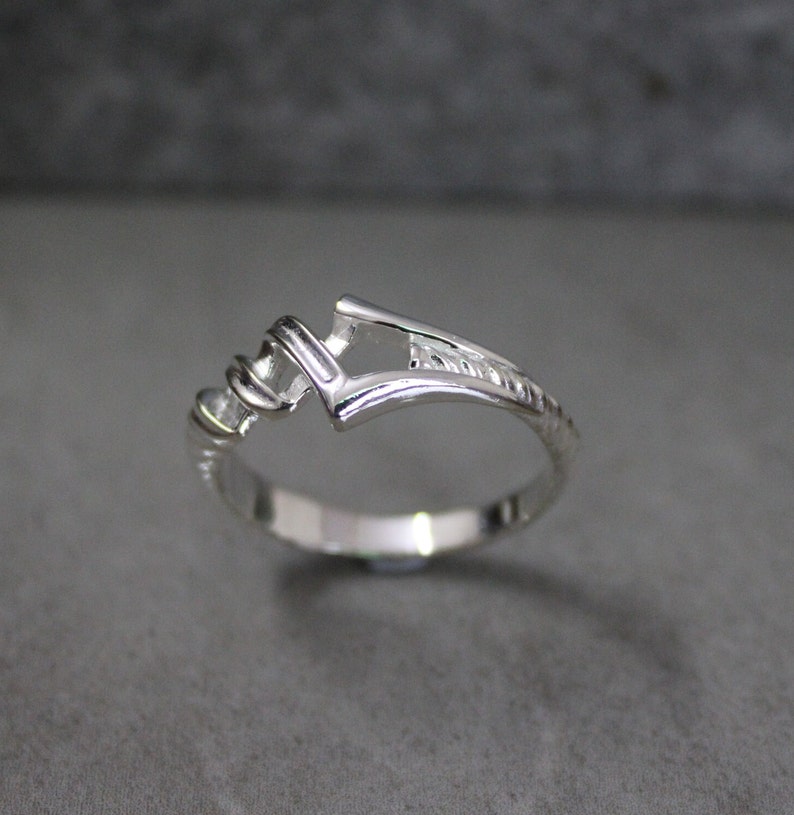 May include: A silver ring with a unique, open design. The band is twisted and has a textured finish.
